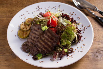 Beef salad: grilled beef steaks with tomatoes, cucumbers, zucchini, lettuce and cabbage, sprinkled with flax seeds. Home made food. Concept for a tasty and healthy meal