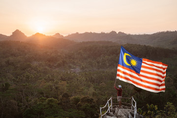 portrait of man on top of the hill in the morning rising malaysia flag celebrating independence day