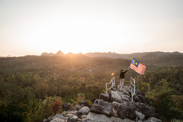 portrait of man on top of the hill in the morning rising malaysia flag celebrating independence day