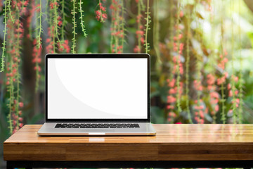 Laptop blank screen on wooden table red flowers green garden