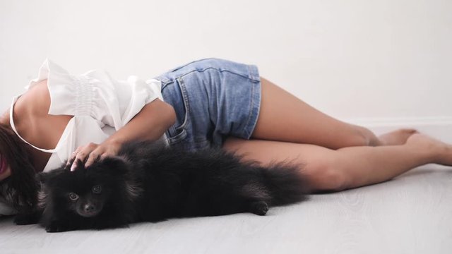 Happy Asian woman lying on floor kissing and touching her black dog with window light, lifestyle concept.
