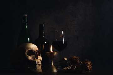 still life of humen skull on table with a glass of wine and wine bottle in a dim light room