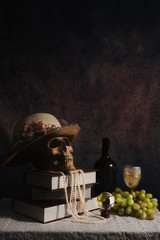 still life of female humen skull wearing lady hat with pearl necklace on books stack on table with...