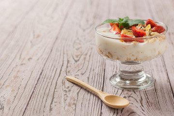 Pieces of fresh strawberries in yogurt with mint on a wooden table.