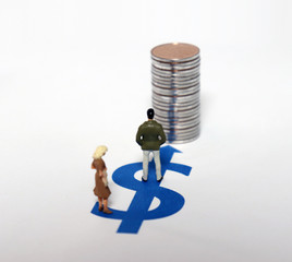 A miniature man and a miniature woman standing on the dollar symbol with a pile of coins.
