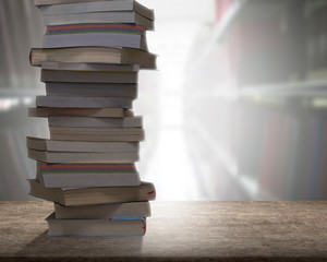 Stacking books on wooden desk with blur bookshelfs background in the library room. Education and knowledge high as a mountain concept.