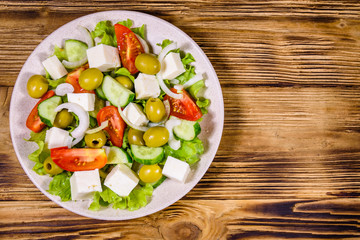 Ceramic plate with greek salad on wooden table. Top view