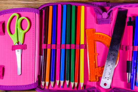 Different school stationeries (pens, pencils, ruler, protractor and scissors) in a pink pencil box. Top view