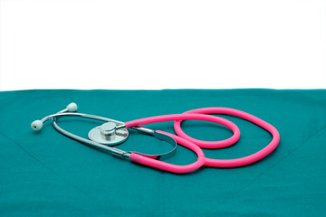 Fototapeta premium Pink stethoscope isolated on surgical green drape background with white space for copy text