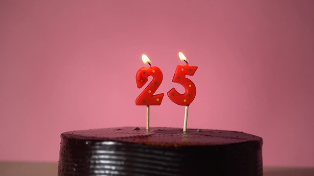 Chocolate birthday cake on pink background with red number twenty five candle in middle electric lighter lighting candle making wish trying to blow out candle  - Powered by Adobe