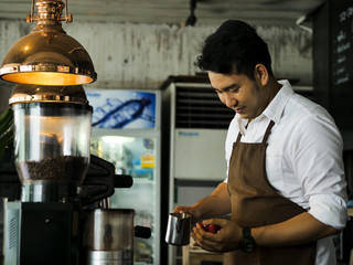 Happy Asian barista pouring milk into red coffee cup for latte art.