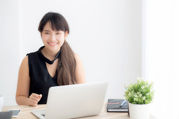 Beautiful freelance asian woman smiling working and typing on laptop computer at desk office with professional, girl using notebook checking email or social network, business and lifestyle concept.