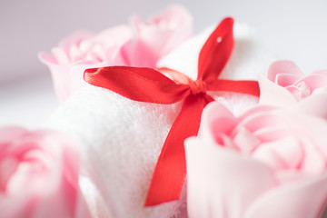 Obraz na płótnie Canvas white towel with red bow and rose soap on white background, body care and cleanliness concept