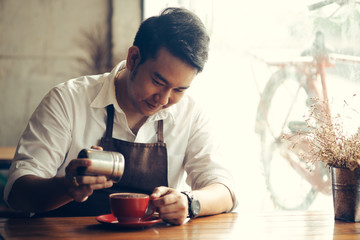 Asian barista sprinkles chocolate powder on drink in red cup.