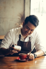 Asian barista sprinkles chocolate powder on drink in red cup.