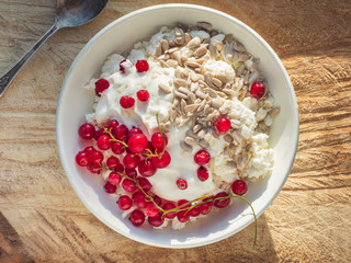 Rustic cottage cheese with seeds and sour cream in a deep white plate on a wooden spile, from the upper angle