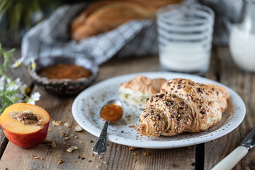 Fresh bread and croissant with milk and peach or apricot jam on a wooden table. Bouquet of daisies. rustic