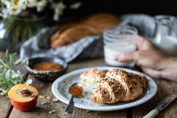 Fresh bread and croissant with milk and peach or apricot jam on a wooden table. Bouquet of daisies. rustic
