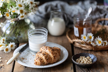 Fresh bread and croissant with milk and peach or apricot jam on a wooden table. Bouquet of daisies. rustic