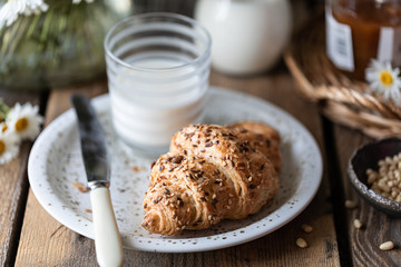 Fresh bread and croissant with milk and peach or apricot jam on a wooden table. Bouquet of daisies. rustic