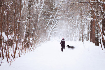 Fototapeta na wymiar Teenager boy with a black labrador retriever in the winter forest.