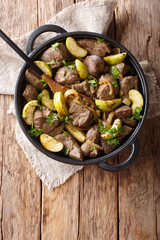 German food fried beef liver with green apples and onions close-up in a pan. Vertical top view