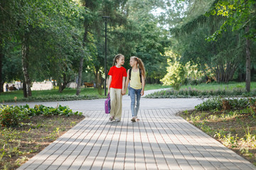 Two teen girls walk along the pavement in the park.