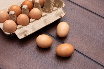 Close up of organic raw chicken eggs in egg box on brown wooden floor background