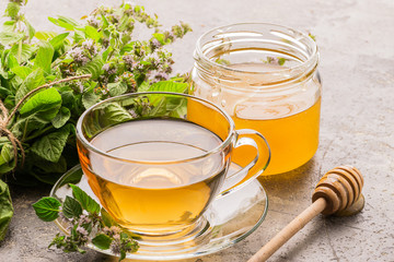 Cup of tea drink with fresh leaves of mint melissa and honey gray background. Healing herbal drink. Horizontal frame.