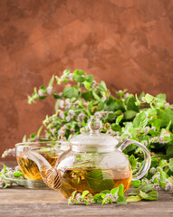 Fresh aromatic tea with melissa mint leaves glass teapot on a rustic background. Healing herbal...