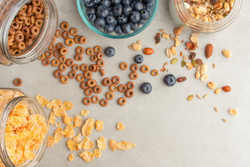 muesli and cereals are scattered with jars with berries of cherries, blueberries and sweet cookies on a light background, breakfast background