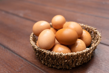 Close up of organic raw chicken eggs in basket on brown wooden floor background