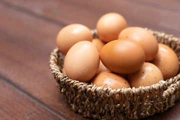 Close up of organic raw chicken eggs in basket on brown wooden floor background