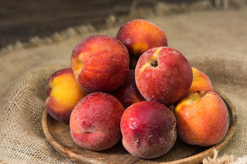 Peaches on a wooden plate on a wooden table. Rustic style