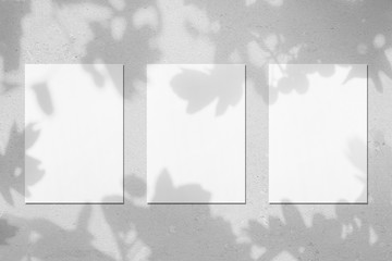 Three empty white vertical rectangle poster mockups with soft shadows on neutral light grey concrete wall background. Flat lay, top view - obrazy, fototapety, plakaty