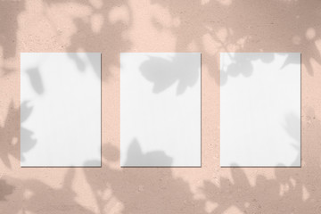 Three empty white vertical rectangle poster mockups with soft shadows on pastel pink colored...