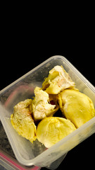 close up of creamy durian fruit inside plastic container isolated in black