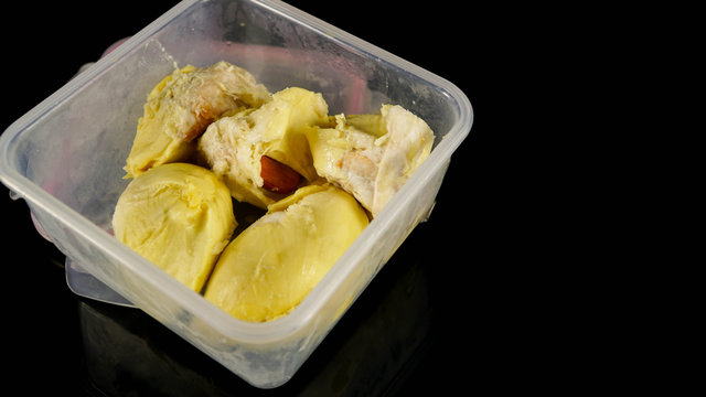 close up of creamy durian fruit inside plastic container isolated in black