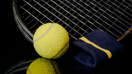 close up of one single tennis ball racket tennis and wrist strap isolated in black with reflection...