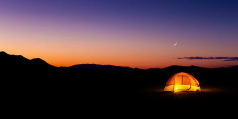 Fototapeta na wymiar Lit Camping Tent at Blue Hour with Crescent Moon in Nevada Desert