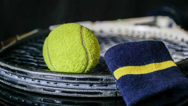 close up of tennis ball racket tennis and black wrist strap isolated in black colour