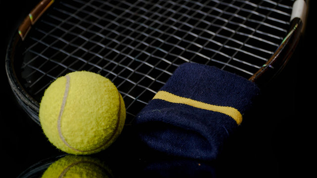 close up of one single tennis ball racket tennis and wrist strap isolated in black with reflection below