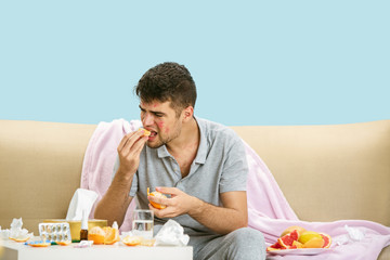 Young man suffering from allergy to citrus fruits. Having skin rash, itching, Sneezing in the napkin, sitting surrounded by grapefruits and oranges. Taking medicine with no result. Healthcare concept.