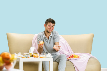 Young man suffering from allergy to citrus fruits. Having skin rash, itching, Sneezing in the napkin, sitting surrounded by grapefruits and oranges. Taking medicine with no result. Healthcare concept.