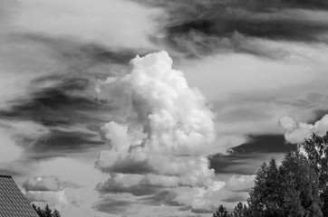 Cumulus cloud is depicted against the background of Cirrus clouds, below you can see a fragment of the roof of the house and a fragment of the tree crown, black and white image, copy space, instagram.