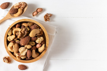 Top view of mixed nuts in a wooden bowl on white background