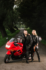 Obraz premium man and woman bikers in leather jackets with sports motor bike on the road in the evening