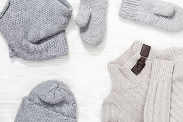 Female knitted cap, scarf, mittens and warm sweater on white wood background with copy space. Autumn and winter clothes for woman. Top view.