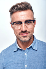 Smart and handsome. Close up portrait of charming bearded man in eyewear looking at camera and smiling while standing against grey background