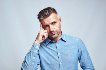 You Are What You Think. Portrait of young and smart bearded man in casual wear touching his head and looking at camera while standing against grey background